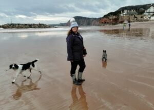 Lady wearing winter clothing, walking on a beach with dogs